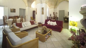 Un salon spacieux doté d’un haut plafond en arc de cercle, d’un canapé rouge, d’un canapé blanc, de fauteuils en osier et d’une table basse.