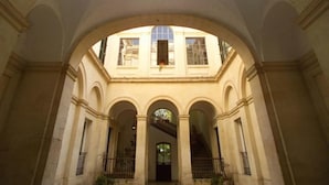 Une cour intérieure agrémentée d’arcades, un escalier central et un bâtiment dont on aperçoit les fenêtres au fond.