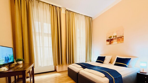 A hotel room with a bed, a desk with a computer, a chair, and a window with curtains. - Pension Liechtenstein (Vienna)