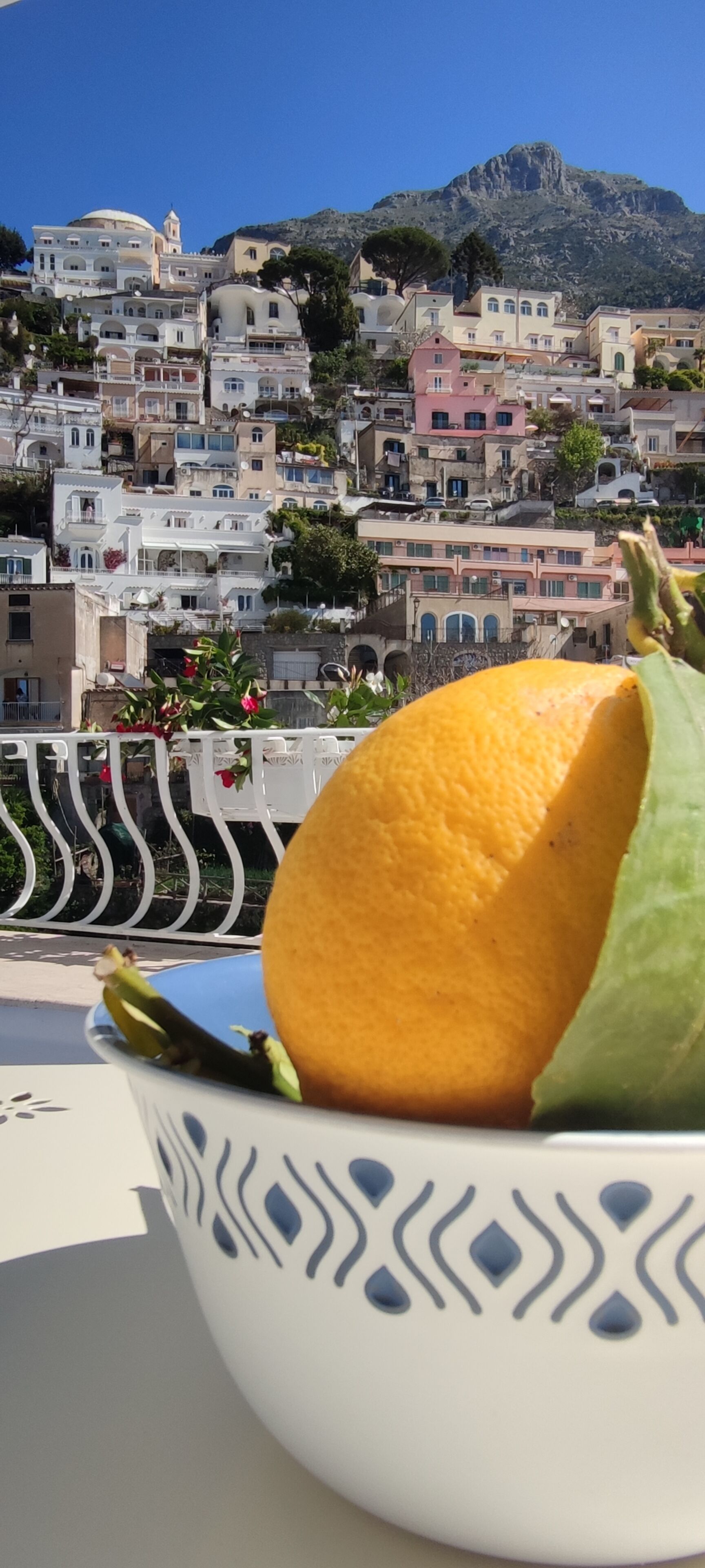 A bowl with a fruit on a balcony overlooking a hillside of buildings.