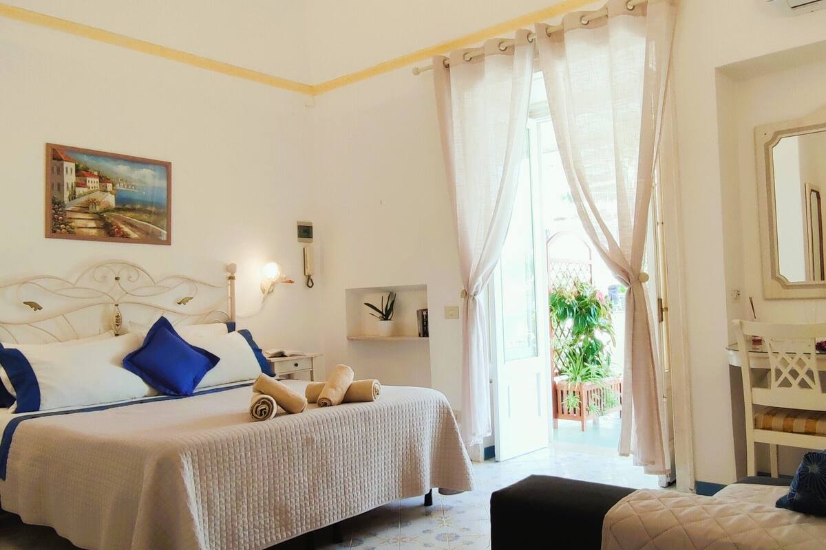 Quarto de hotel com cama, mesa de cabeceira, luminária e um espelho grande.