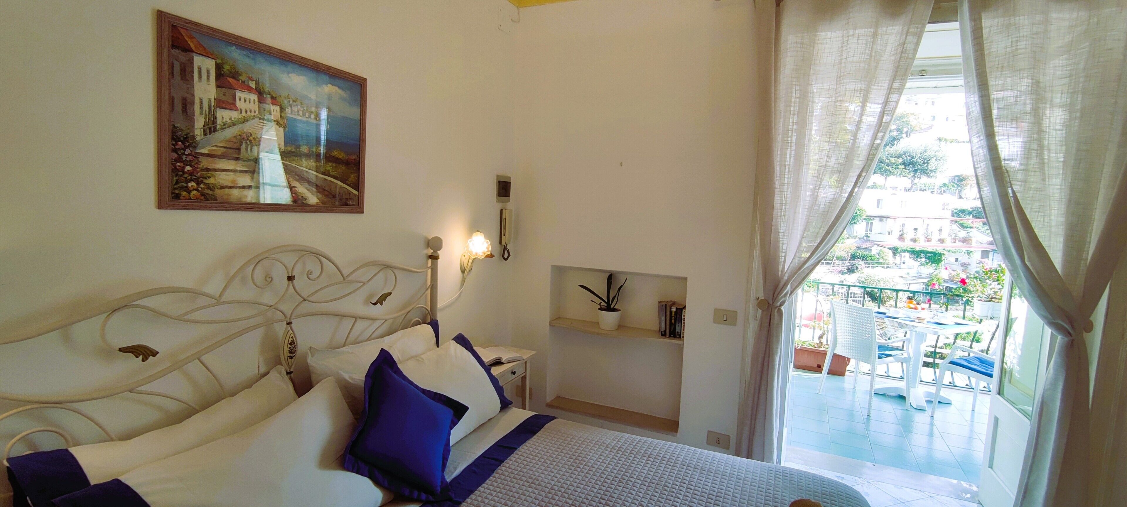 A bedroom with a bed, bedside table, lamp, and a painting on the wall.