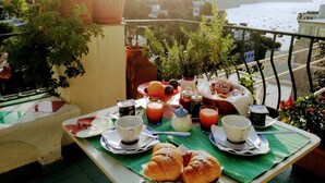 Ein Balkon mit Frühstückstisch, ausgestattet mit Croissants, Kaffee und Saft, mit Blick auf eine Küstenstadt.