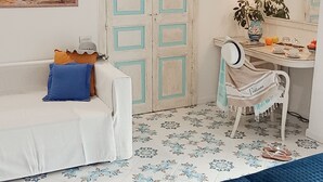 Ein Zimmer mit einem weißen Sofa, einem Schreibtisch mit Stuhl, einem Bett, einem Gemälde und einem gemusterten Boden.