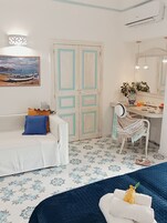 Una habitación con un sofá blanco, un escritorio con una silla, una cama, un cuadro y un suelo con estampado.