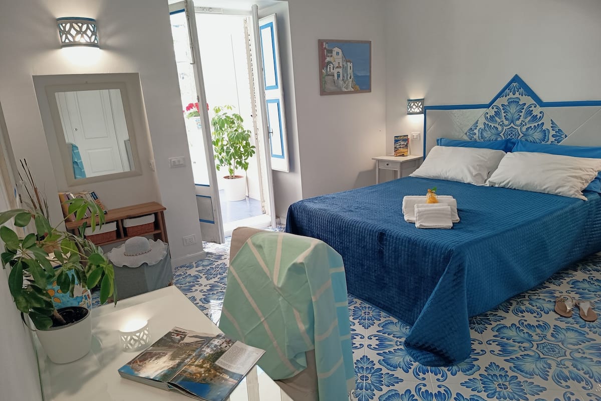 Quarto com cama, mesa de cabeceira, luminária e vista para o exterior.