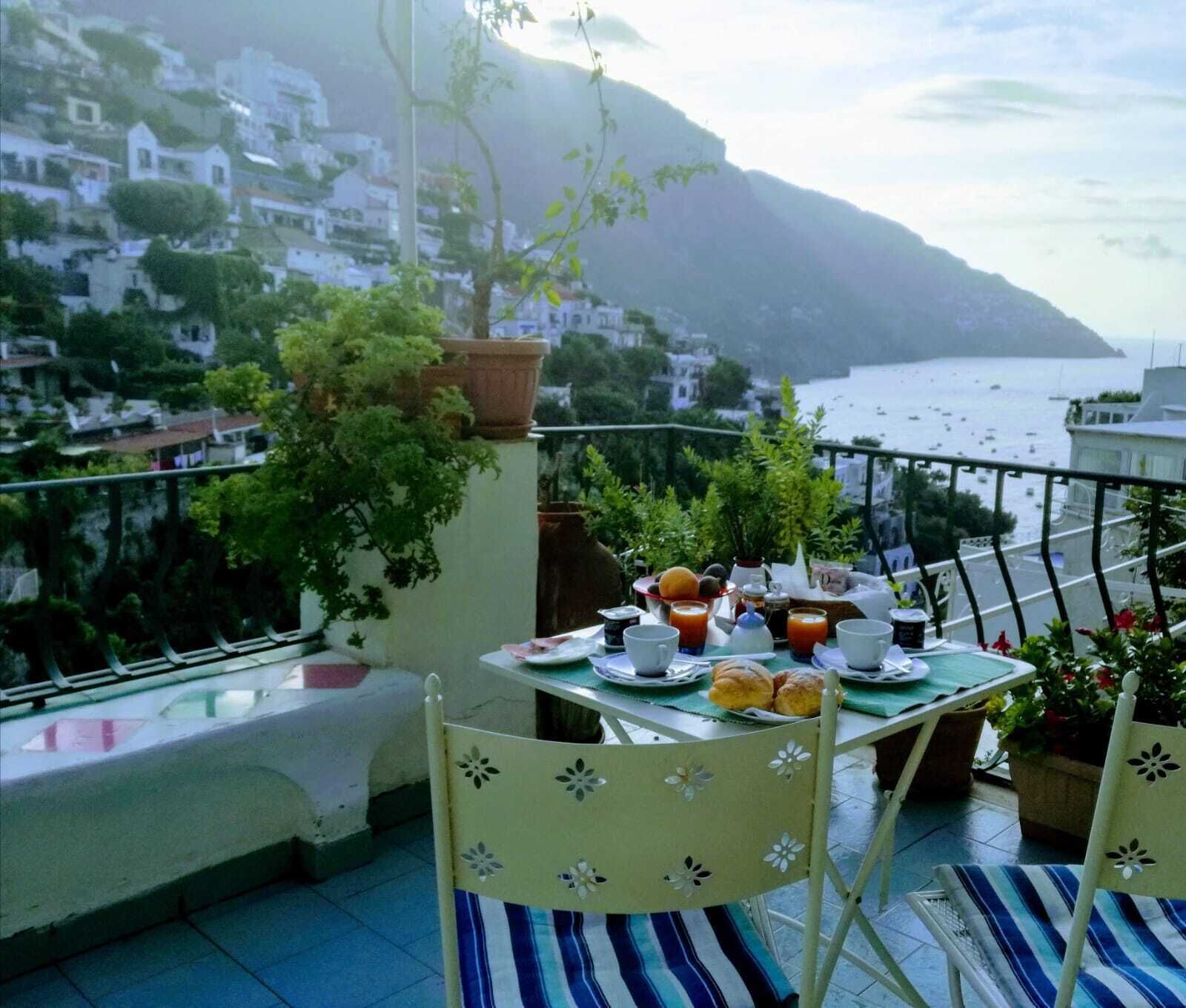 Un balcón con una mesa lista para el desayuno, con vistas a un pueblo costero y al mar.