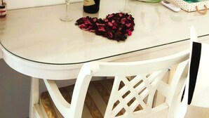 Ein Essbereich mit Tisch, Stühlen, einem Spiegel, einer Champagnerflasche, einem Glas, einem Wasserkocher und einem Tablett mit Flaschen.