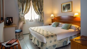 A hotel room with a bed, two bedside lamps, a chair, a desk with a lamp, a framed picture on the wall, and a window with curtains. - Marini Park Hotel (Rome)