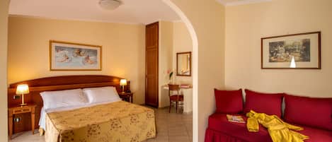 A hotel room with a bed, a red sofa, a desk, and two paintings on the walls.