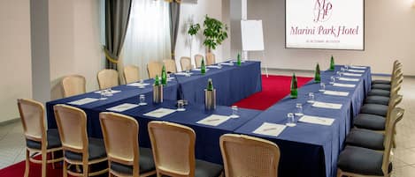 A conference room with a long table, chairs, and a projector screen displaying the hotel's name.