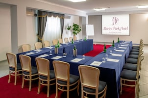 Egy konferenciaterem, melyben egy hosszú asztal, székek és egy projektorvászon található, amelyen a szálloda neve látható.