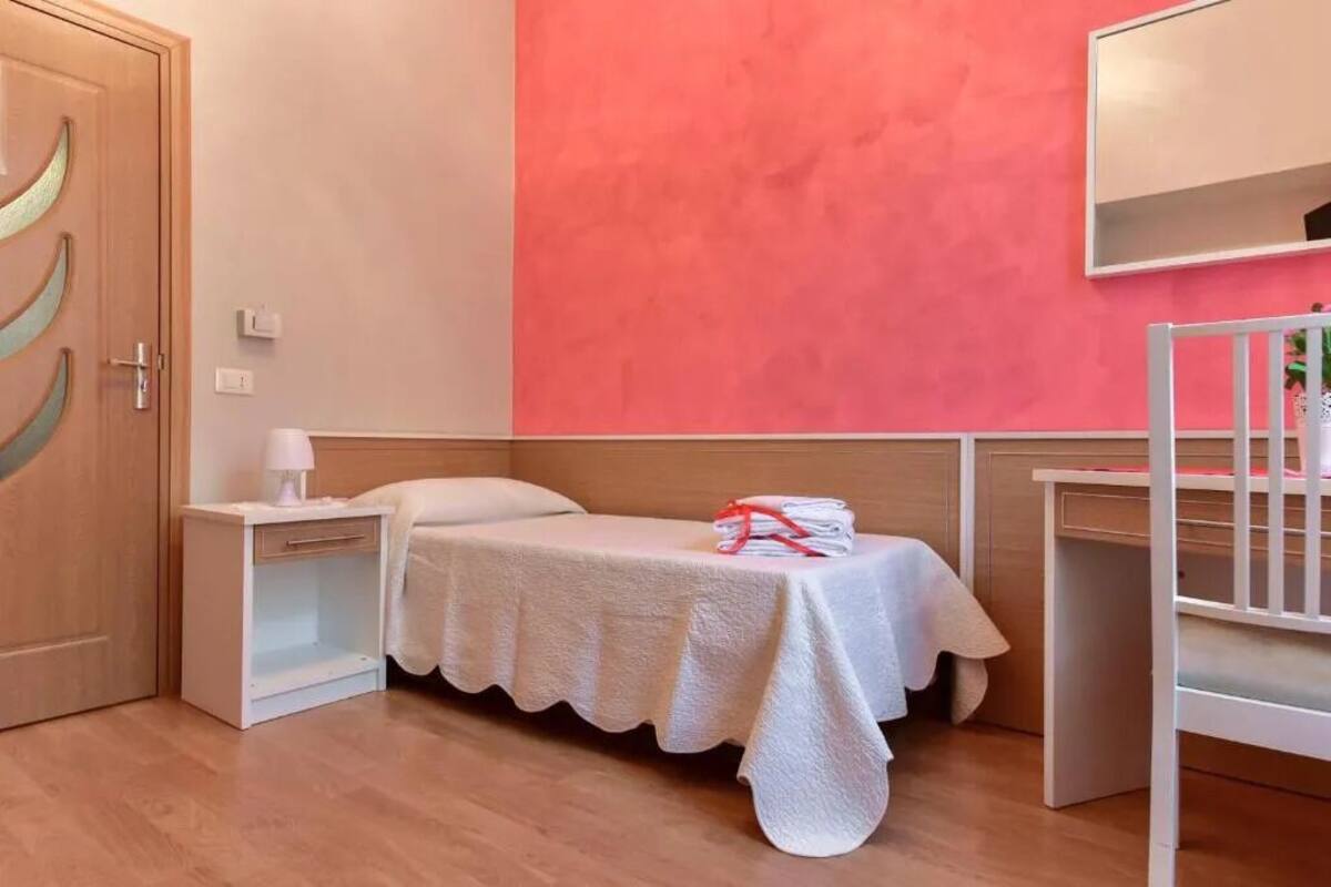 A room with a bed, a nightstand, a crib, and a mirror on the wall.