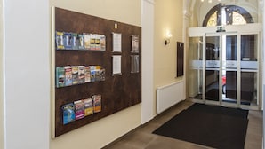 A reception area with a bulletin board displaying various magazines and a glass door entrance. - Hotel Petr (Prague)