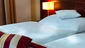 A neatly made bed with white linens and a red and white striped pillow. - Hotel Petr (Prague)