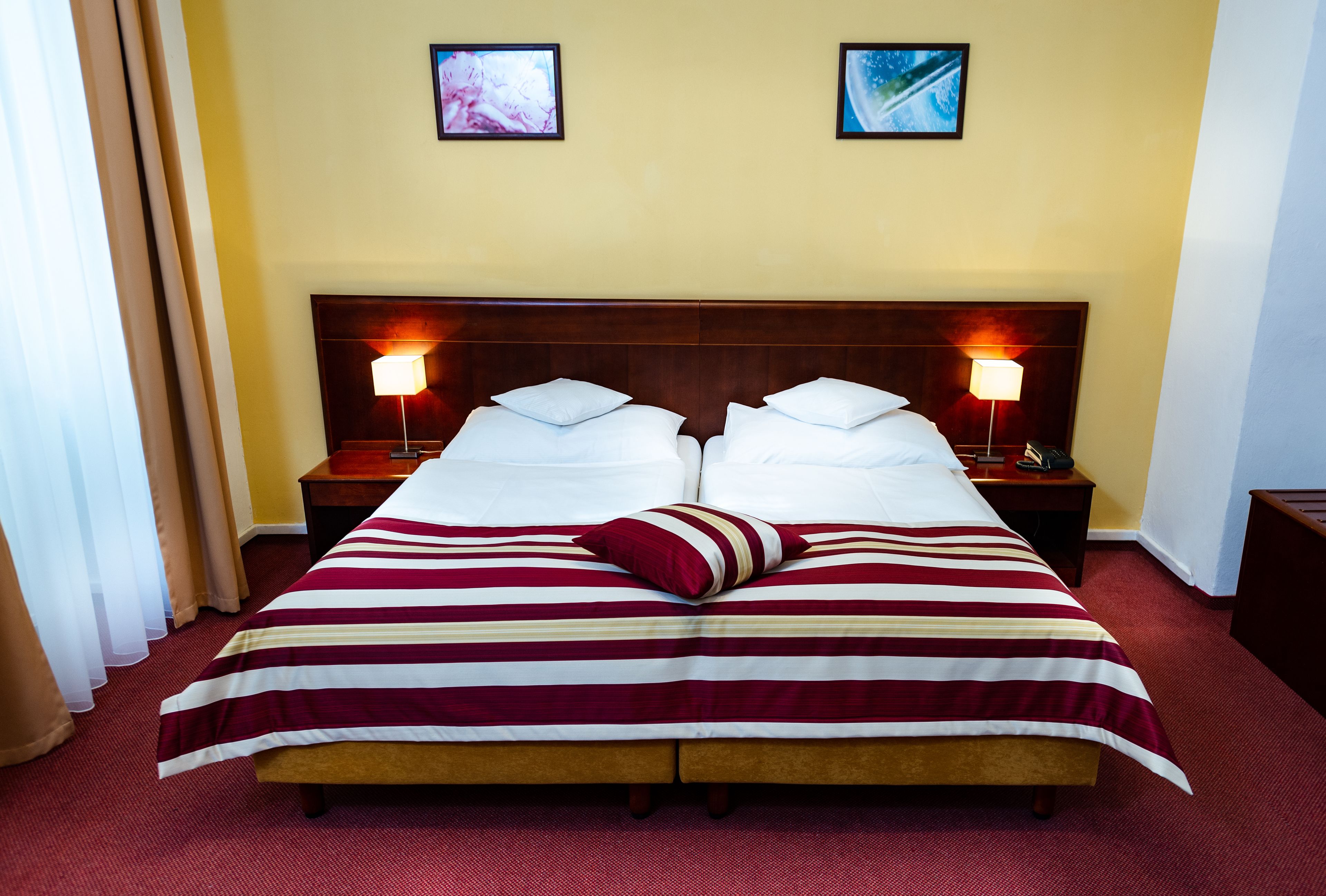 Een tweepersoonsbed met een gestreept beddegoed, twee nachtkastjes met lampen, en twee ingelijste foto's aan de muur.