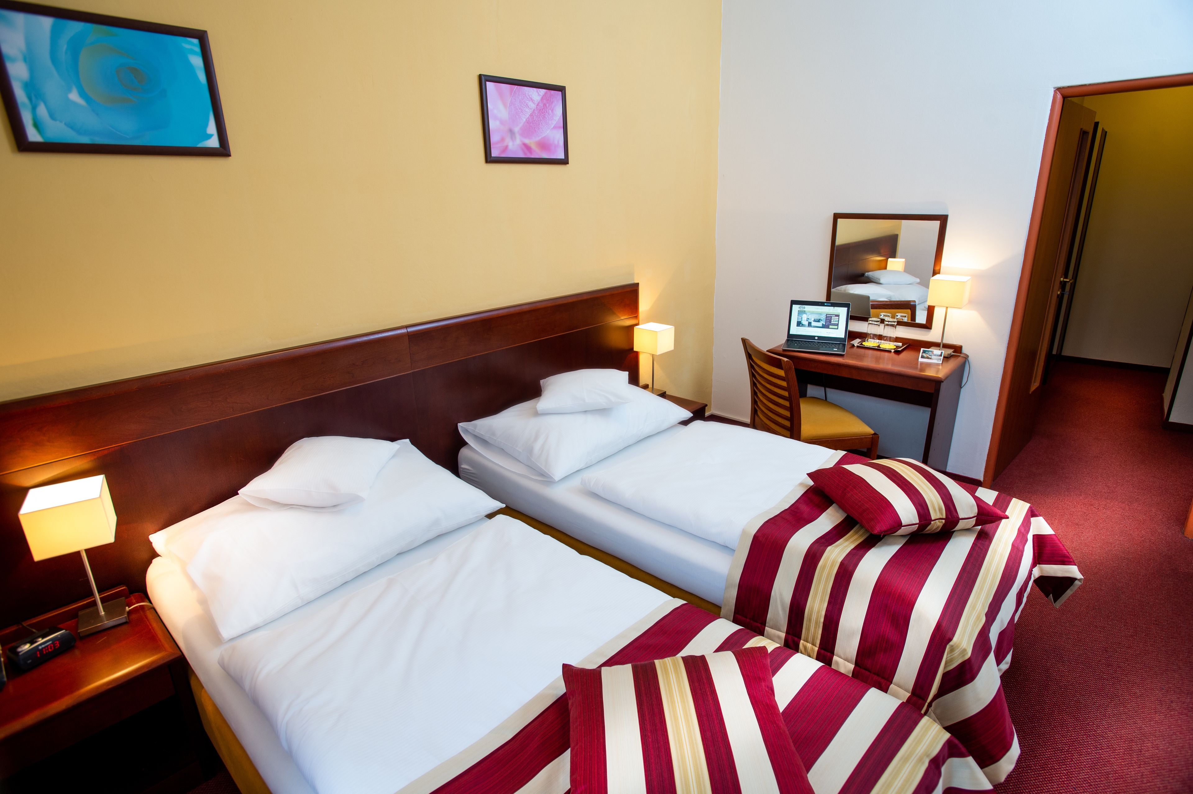 Hotellihuone, jossa on kaksi sänkyä, työpöytä, jossa on kannettava tietokone, tuoli ja peili.