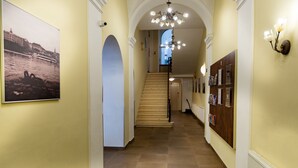 A hallway with a staircase, a chandelier, and framed pictures on the walls. - Hotel Petr (Prague)