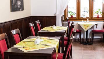 Una sala ristorante con tavoli in legno e sedie rosse imbottite, apparecchiata con tovaglie e posateria.