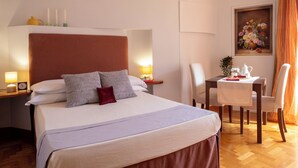 Habitación de hotel con una cama grande, mesitas de noche con lámparas, una pequeña mesa con tetera y un cuadro en la pared.