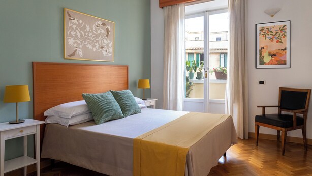 Habitación de hotel con cama, dos mesitas de noche con lámparas, una silla y obras de arte en las paredes.