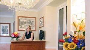 A reception area with a wooden desk, a chandelier, framed pictures on the wall, and a vase of flowers.