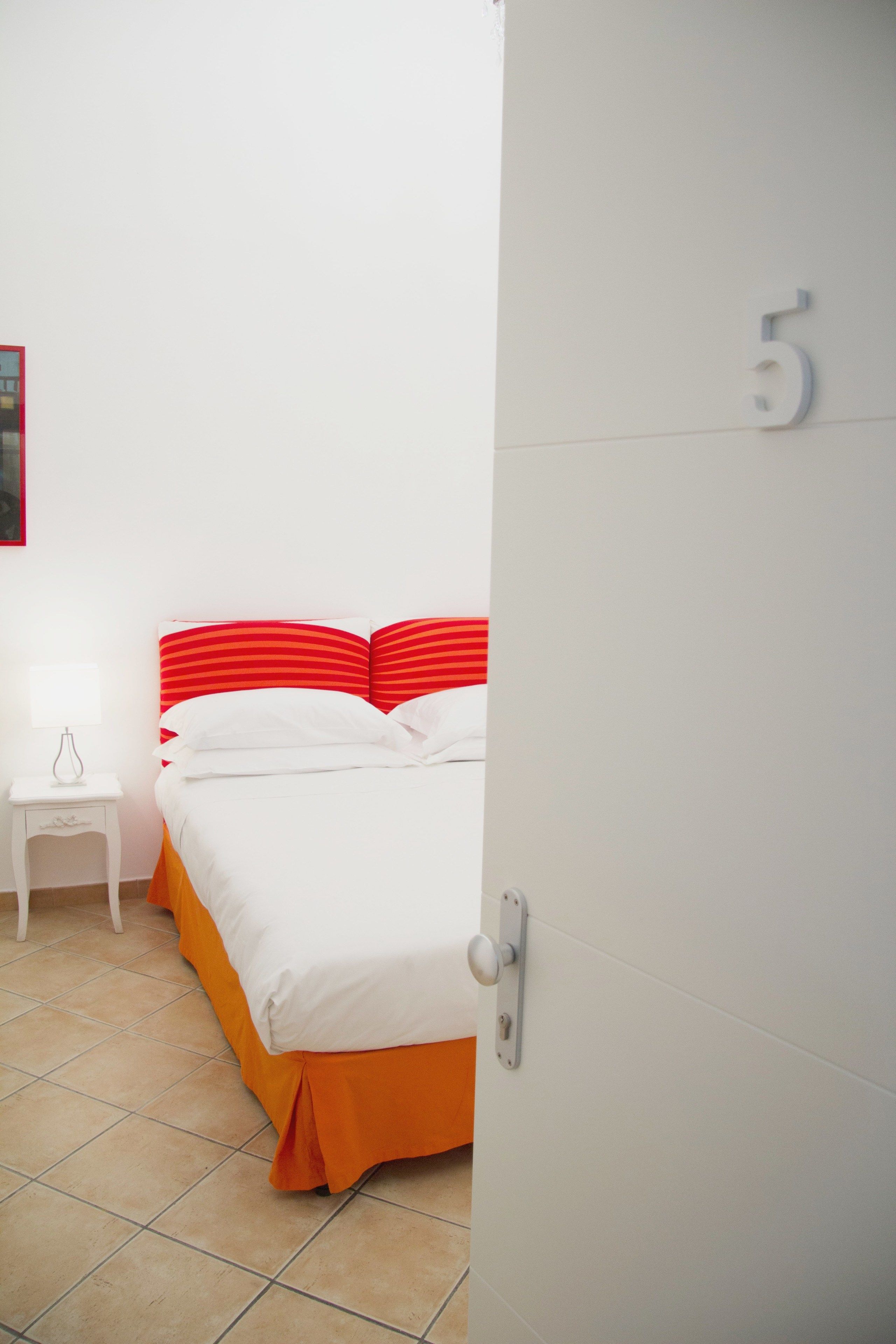 A hotel room with a bed, a nightstand, and a door with the number 5.