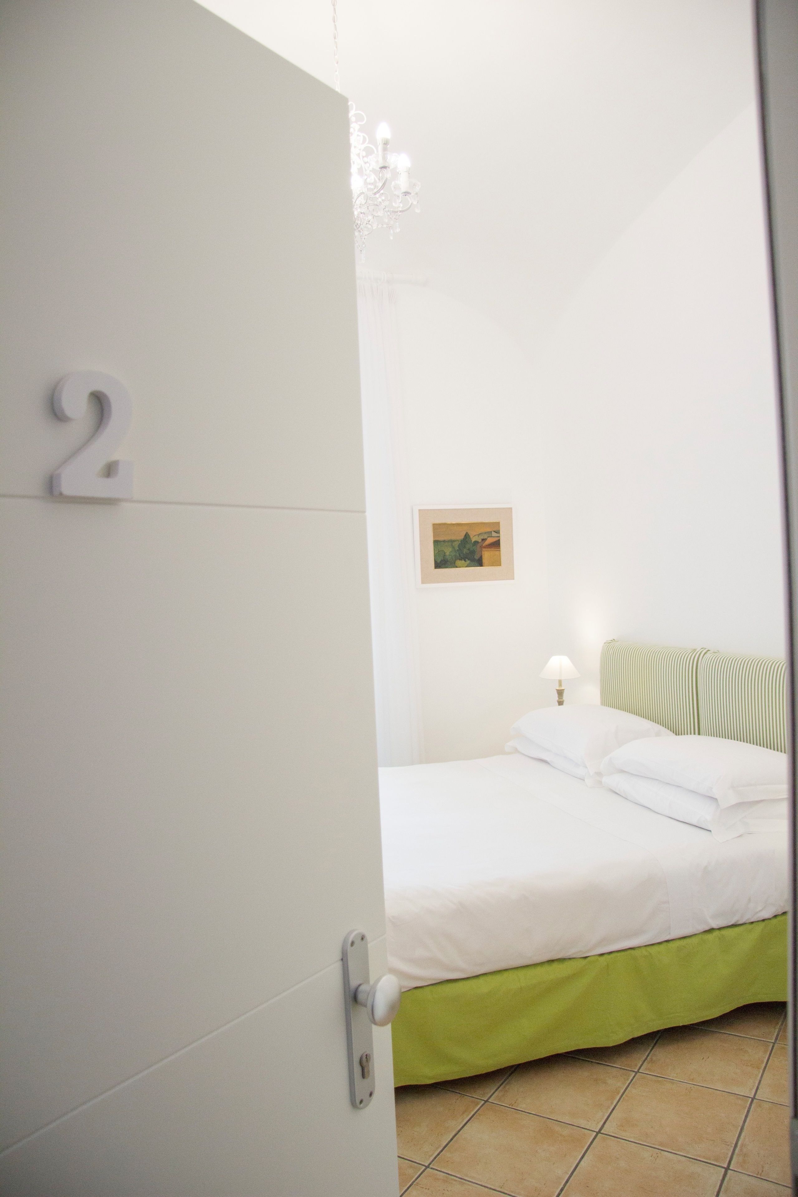 Ein Schlafzimmer mit einem Bett, einem Nachttisch, einer Lampe, einem Bild an der Wand und einer Tür mit der Nummer 2.