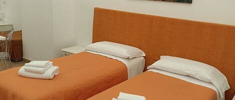 Quarto de hotel com duas camas, cada uma com colcha laranja e almofadas brancas, e um quadro de flores na parede.