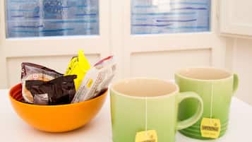 A window with a view of a sailboat on water, a bowl with snacks, and two green mugs on a table.