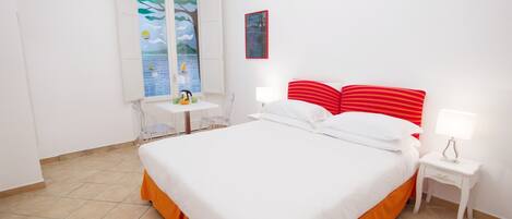 A hotel room with a bed, a desk, a chair, a window with a view, and a wall-mounted air conditioner.