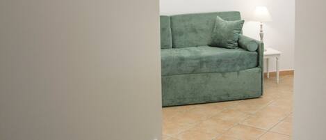 Una habitación con un sofá verde, una araña y cuadros enmarcados en la pared.