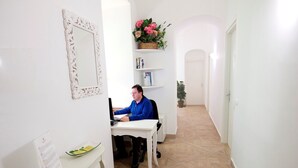 Une pièce comprenant un bureau, une chaise, un ordinateur, un miroir, une plante en pot et une petite table sur laquelle est posé un vase de fleurs.