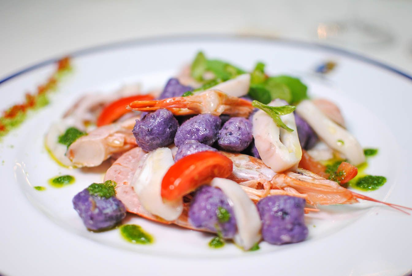 A seafood dish with shrimp, purple balls, and red peppers on a plate.