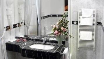 A bathroom with a black and white marble sink, a white vase with flowers, and a white towel rack.
