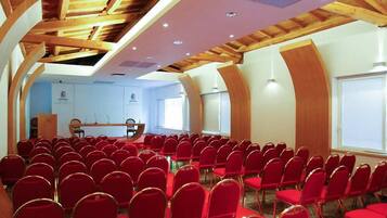 A conference room with red chairs arranged in rows, a stage with a podium, and a high wooden ceiling with skylights.