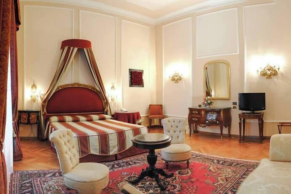 Um quarto espaçoso com uma cama de dossel, televisão, penteadeira com espelho e colcha listrada em vermelho e branco.