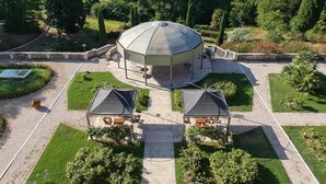 Un gran pabellón abovedado rodeado de jardines cuidados y senderos, con montañas al fondo.