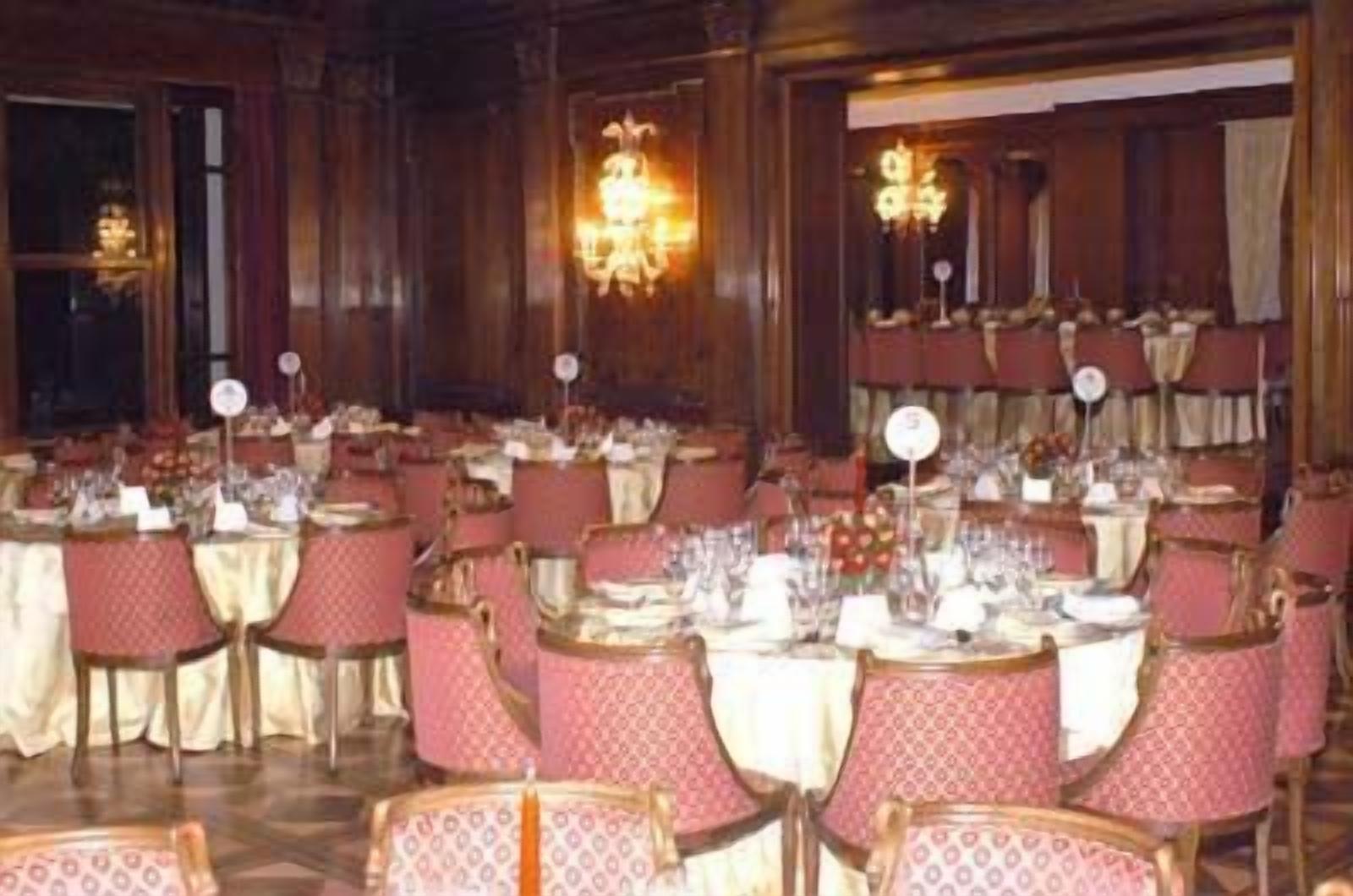 A banquet hall with round tables set for dining, each with a white tablecloth and red chairs.