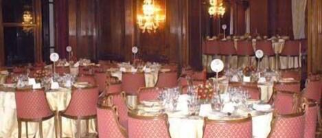 A banquet hall with round tables set for dining, each with a white tablecloth and red chairs.
