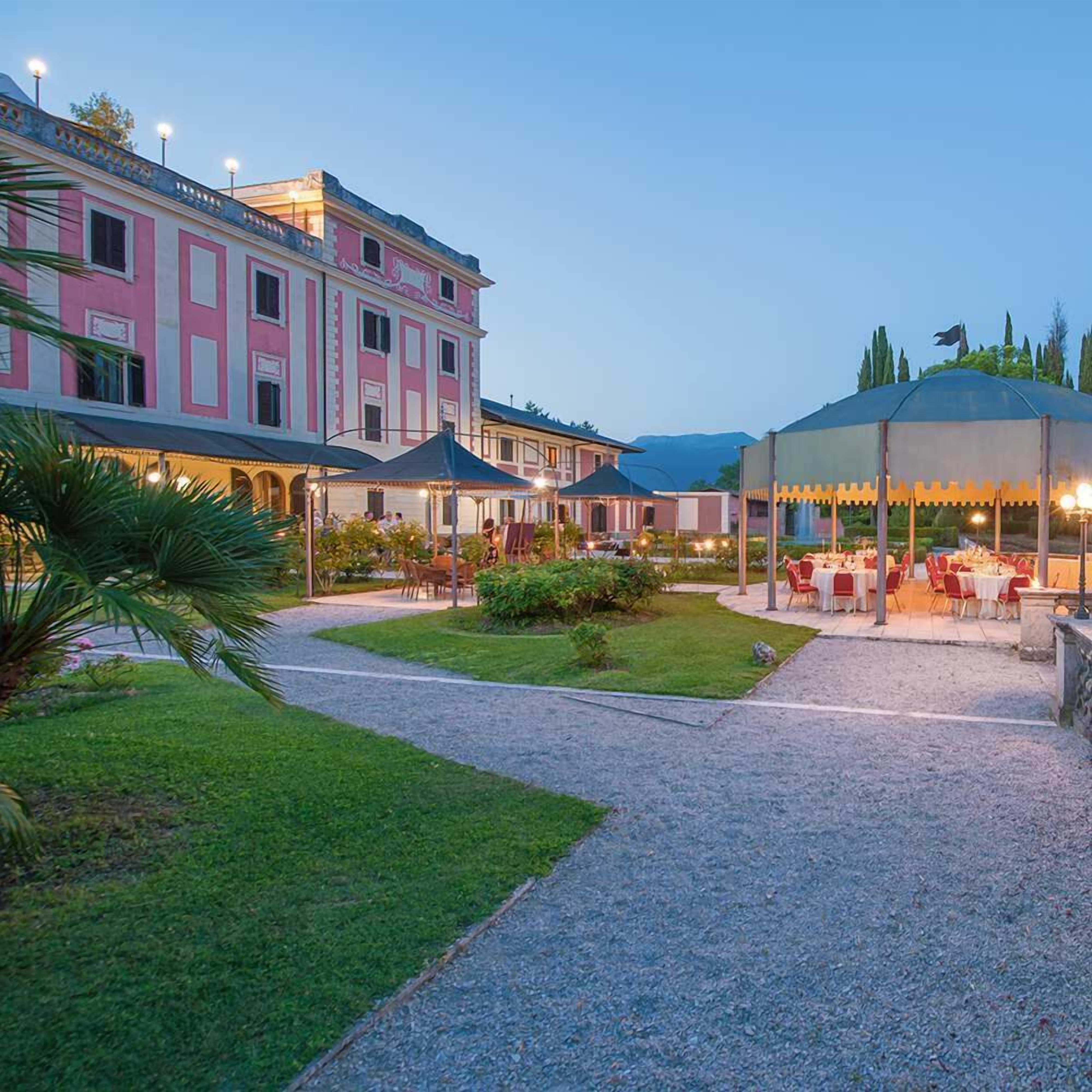 A courtyard with a covered dining area, a building with pink and white facade, and a gravel path.