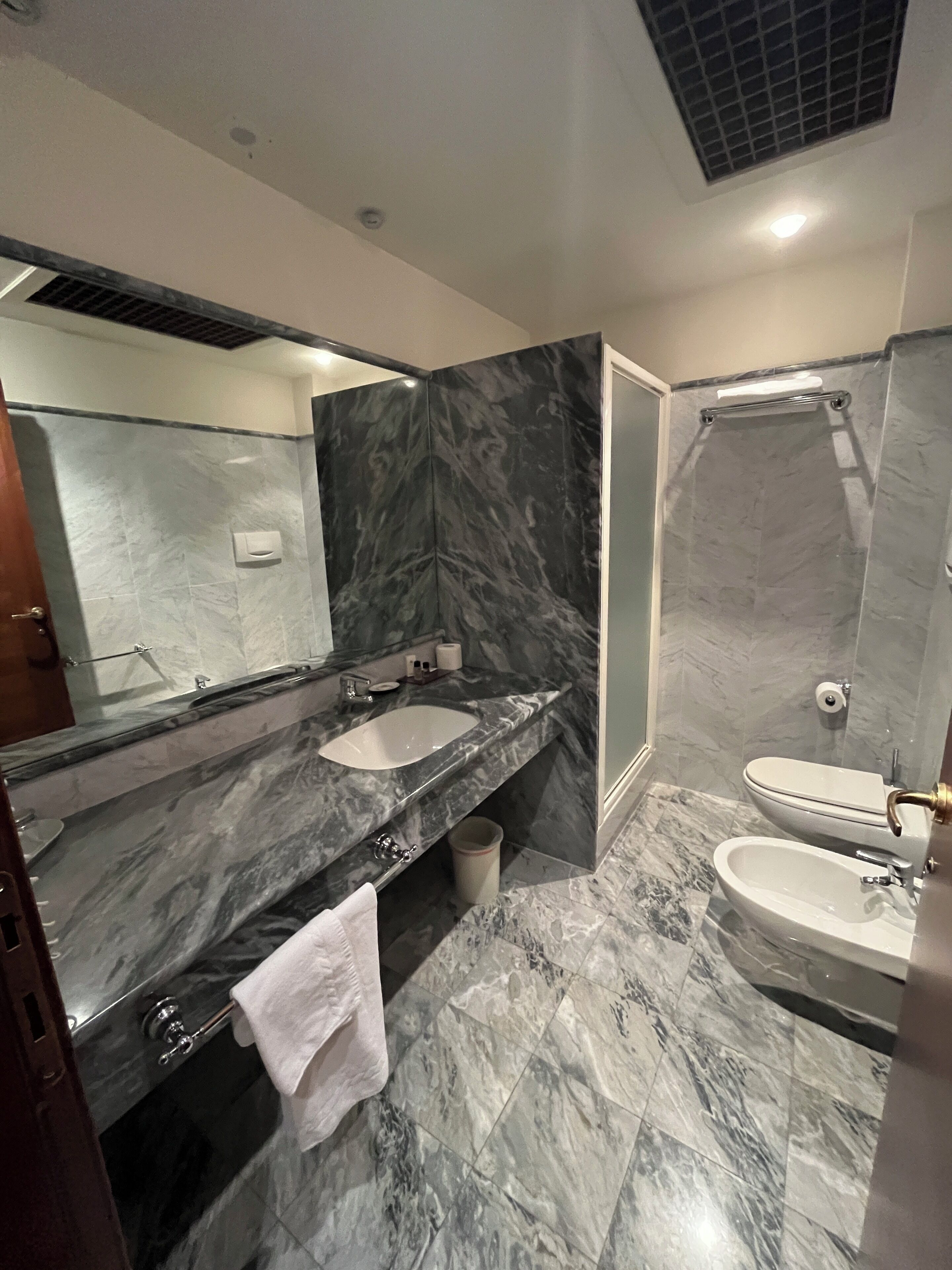A modern bathroom with a marble vanity, a separate sink, a toilet, and a shower area.