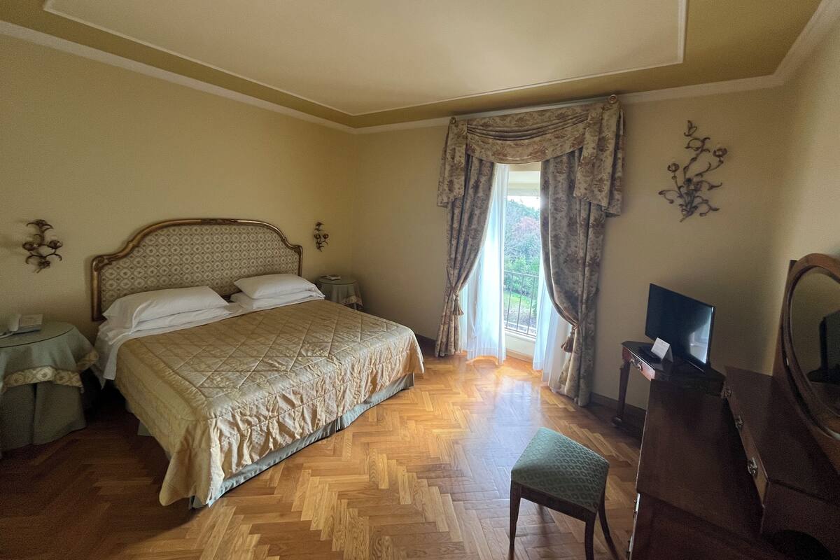 Quarto com cama, escrivaninha, cadeira, espelho e janela com cortinas.