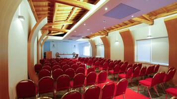 A conference room with rows of red chairs, wooden ceiling beams, and a stage with a podium.