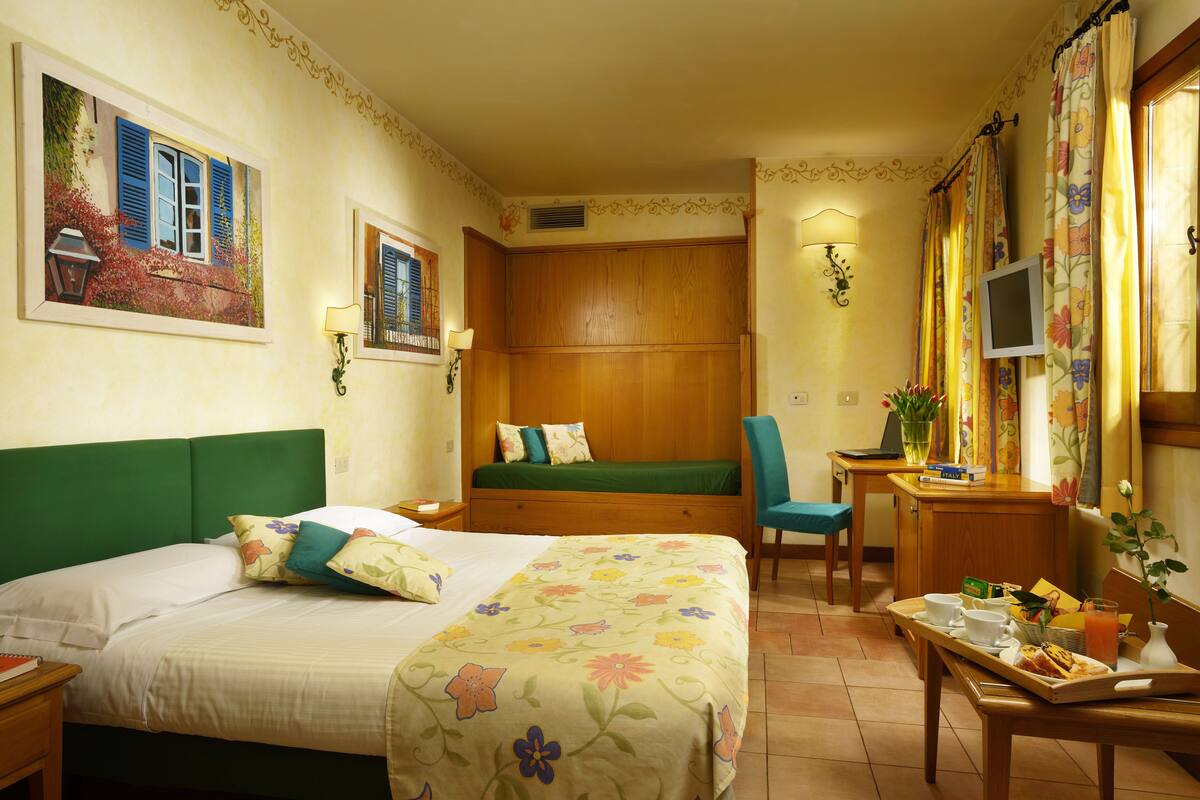 A hotel room with a bed, a desk, a chair, and a small table with breakfast items.