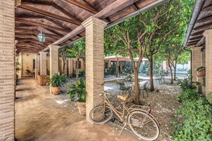 A covered patio area with brick flooring, a bicycle, and outdoor seating under trees.