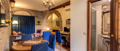 Un comedor con mesa y sillas de madera, una araña y una pared de piedra.