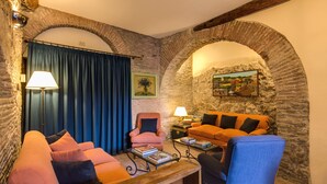 A cozy living room with stone walls, a blue curtain, and a mix of orange and blue sofas. - Hotel Santa Maria (Rome)