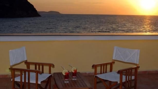 Una terraza con dos sillas de madera y una mesa, con vistas a un atardecer sobre el mar.
