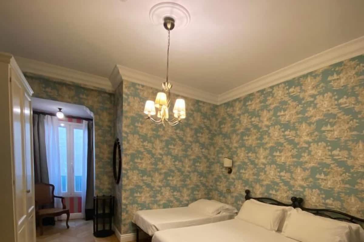 A bedroom with two single beds, a chandelier, and a herringbone-patterned floor.